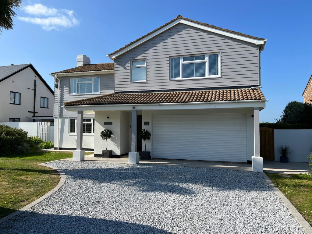 Detached home in Sussex finished in pale grey render and cladding under a clear blue sky